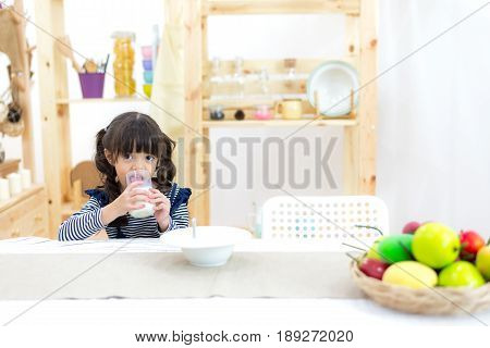 Cute little girl with milk mustache holding glass of milk