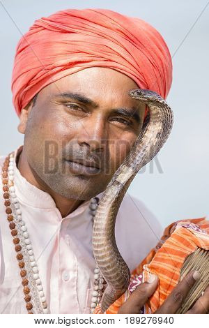 POKHARA NEPAL - OCTOBER 07 2016 : Portrait of snake charmer adult man in turban and cobra sitting near the lake