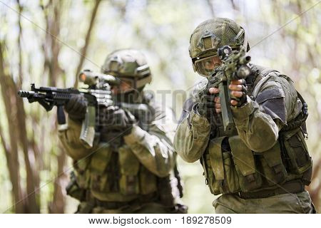 Military men with weapons on reconnaissance in forest