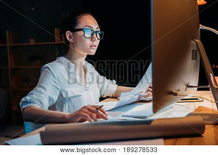 Young Concentrated Asian Businesswoman In Eyeglasses Working With Documents And Computer
