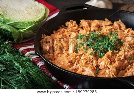 Delicious stewed cabbage in iron pan on dark rustic background with the ingredients for this dish. vegetarian food