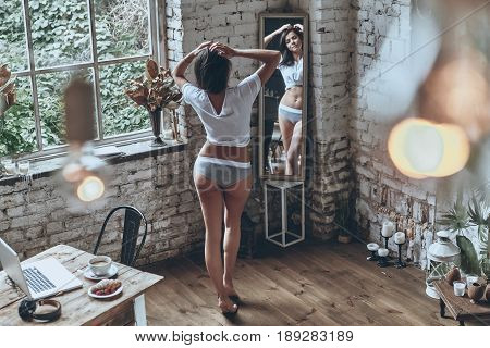 Used to look perfect. Full length rear view of attractive young woman looking in the mirror while spending free time at home