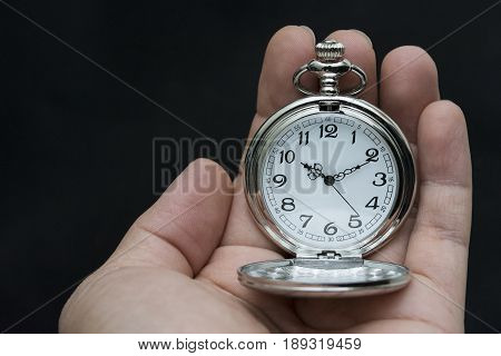 Male hand holding antique pocket watch. Isolated on black background.