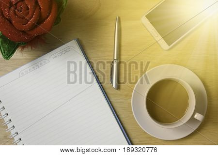 Simple workplace with a cup of coffee notebook paper pen smartphone and glasses on wood table