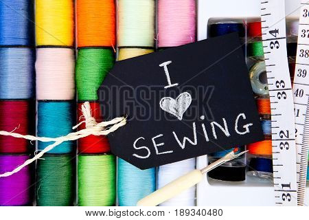 I love Sewing - colorful cotton reels background with blackboard and tape measure and unpicker