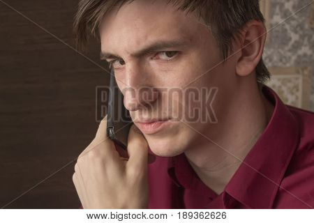 young man in a purple shirt is waiting for an answer on a black smartphone, with an alarming suspicious look