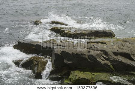 Waves crash over large boulders along the shoreline in Newport Rhode Island