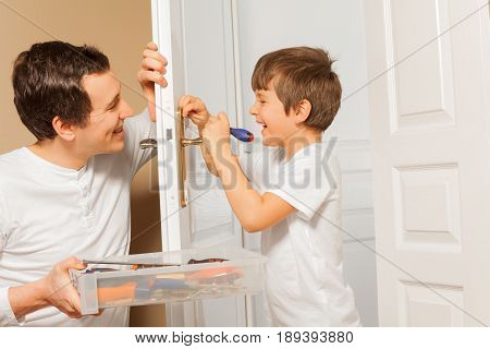 Happy young man holding tool box and helping his kid son to draw up a bolt of door handle at home