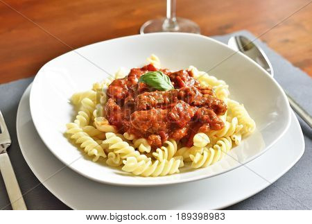 Delicious goulash dish on a white plate with basil leaf. Spiral pasta with tomato sauce.