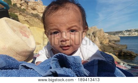 two months old baby boy laying on stomach on rocki beach