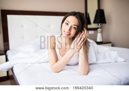 Woman Lying At The End Of The Bed Underneath The Quilt And Smiling, With Her Head Resting Upon Her H