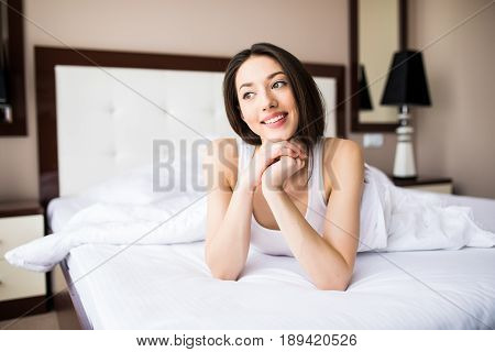 Woman Lying At The End Of The Bed Underneath The Quilt And Smiling, With Her Head Resting Upon Her H