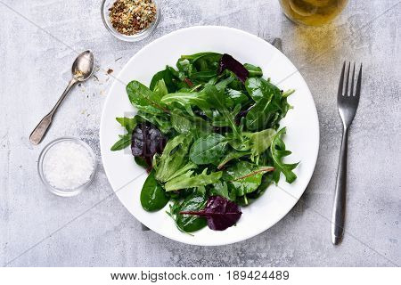 Salad with green leaves of spinach arugul on light stone background. Healthy natural food top view
