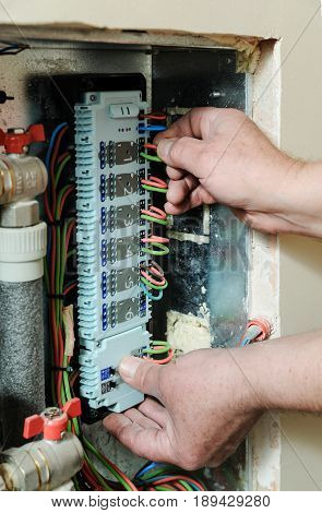 Electrician's hands are inserting wires in a switch for thermostats and servo drives valves in a home heating system.