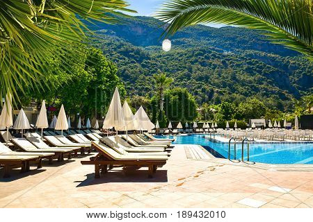Sunny Hotel Resort with luxury blue swimming pool palm trees umbrellas and sunbeds in Turkey. Rich vacation on the sunny resort.