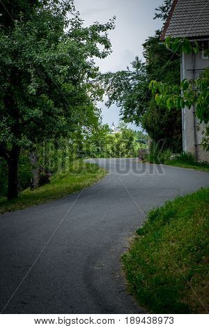 Winding asphalted road leading to the church on the hill. Countryside village landscape with rural house. Rural road inside of village.