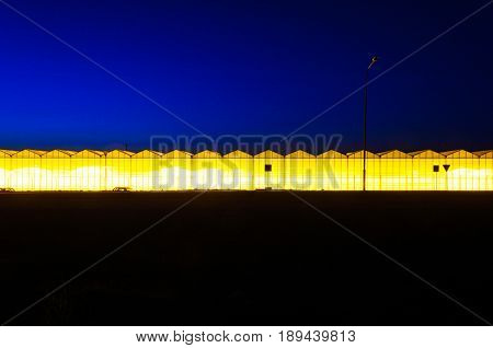 Greenhouse plant at night. Night landscape luminous glass construction. Silhouette of road signs on a background of a facade of a hothouse