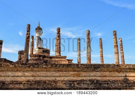 Ancient Buddha statue sitting posture among the ruins pillars under the blue sky at Wat Maha That temple in Sukhothai Historical Park is an old city and famous attractions Thailand