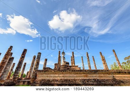 Ancient Buddha statue sitting posture among the ruins pillars under the blue sky at Wat Maha That temple in Sukhothai Historical Park is an old city and famous attractions Thailand