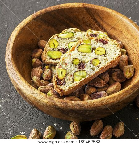 Traditional crispy Italian biscotti or cantuchini crackers with pistachios and dried cranberries in a bowl of olve wood on a dark background. Home classic healthy food