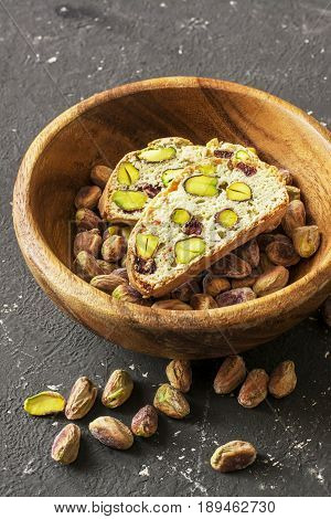 Traditional crispy Italian biscotti or cantuchini crackers with pistachios and dried cranberries in a bowl of olve wood on a dark background. Home classic healthy food