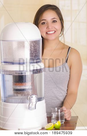 Beautiful girl behind a filter system of water purifier on a kitchen background.