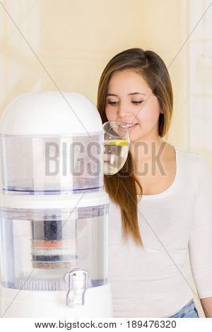 Beautiful woman drinking a glass of water with a filter system of water purifier on a kitchen background.