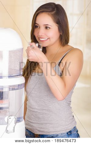 Beautiful woman drinking a glass of water with a filter system of water purifier on a kitchen background.
