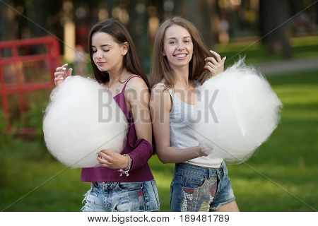 Two young women sharing cotton candyfloss at amusement park. Best friends eating cotton candy together outdoors.