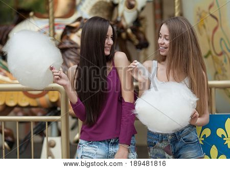 Two young women sharing cotton candyfloss at amusement park. Best friends eating cotton candy together outdoors.