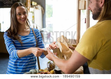 Smiling female customer paying bill by cash at bread counter in bakery shop