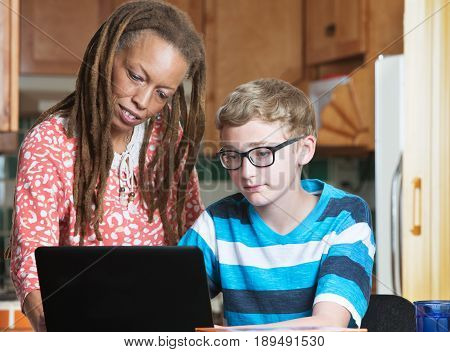 Foster parent helping child in eyeglasses working on laptop