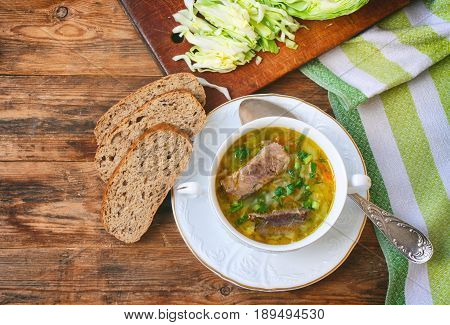 Cabbage soup shchi with fresh cabbage with beef with herbs in white bowl on plate towel slices of cereal bread on wooden table Russian cuisine