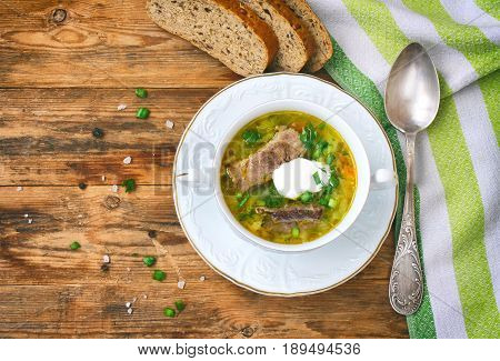 Cabbage soup shchi with beef and sour cream in white bowl on plate grain bread on wooden table traditional Russian cuisine