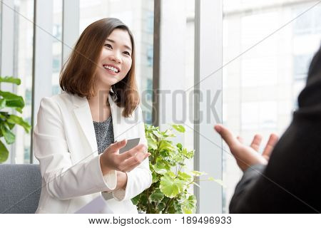 Smiling confident Asian business woman talking with client in ofiice lounge