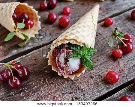homemade ice cream cherries and chocolate in a waffle cone, fresh cherries on old wooden table - left view