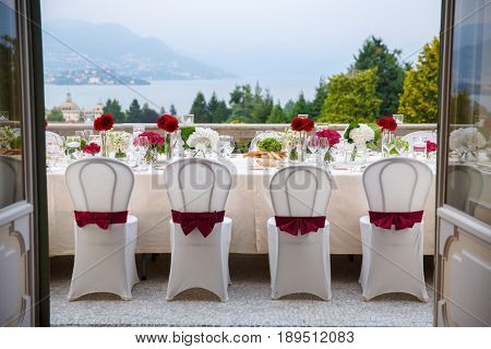 Decorated with red bows and cassets a dining table on the balcony awaits guests. From the balcony you can see the lake at the foot of the Alpine mountains