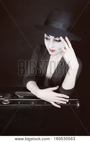 The woman mime sits next to the suitcase waiting for the trip. Theatrical Performance