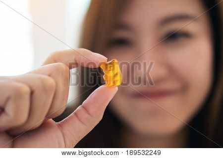 Closeup image of a beautiful Asian woman smiling holding and looking at orange gummy bear