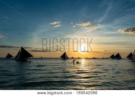 BORACAY, WESTERN VISAYAS, PHILIPPINES - MARCH 24, 2017: Bright yellow sunset over the sea. Some sailboats and a stand up paddle have great view.