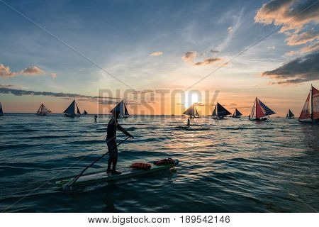 BORACAY, WESTERN VISAYAS, PHILIPPINES - MARCH 24, 2017: Wide angle view from the beach, looking the amazing sunset in Boracay. Stand up paddle, sailing boats makes this colorful sunset more beautiful