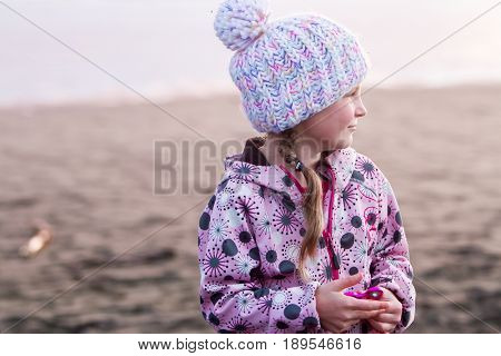 outdoor portrait of young happy smiling child girl in knitted hat on outdoor natural background