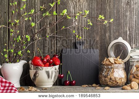 A simple home kitchen still life with ingredient for a healthy breakfast, cereal flakes, strawberries on a dark wooden aged background.
