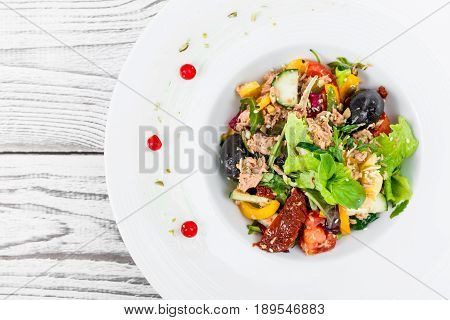 Fresh salad with tuna arugula artichokes codfish olives basil sun dried tomatoes cherry tomatoes cucumber cauliflower on wooden background close up. Mediterranean food. Top view
