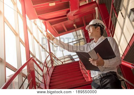 Young Asian Engineer or Architect holding files while wearing personal protective equipment safety helmet at construction site. Engineering Architecture and building construction concepts