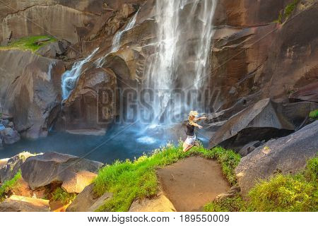 Hiking woman jumping in Yosemite National Park at Vernal Fall on Merced River from Mist Trail. Cheering happy hiker enjoying view of beautiful waterfalls. Summer travel holidays in California, USA.