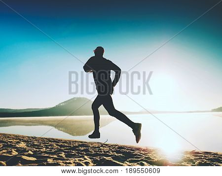 Healthy Lifestyle. Tall Young Man Runner Is Running On Sunrise Seaside. Man Jump In Sand