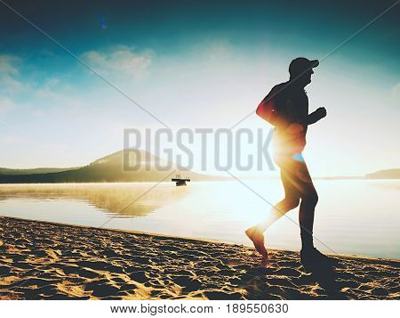 Healthy Lifestyle. Tall Young Man Runner Is Running On Sunrise Seaside. Man Jump In Sand
