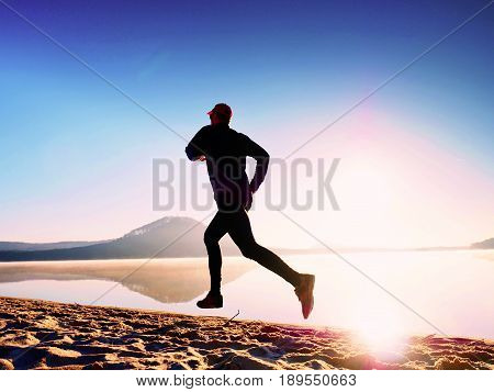 Healthy Lifestyle. Tall Young Man Runner Is Running On Sunrise Seaside. Man Jump In Sand