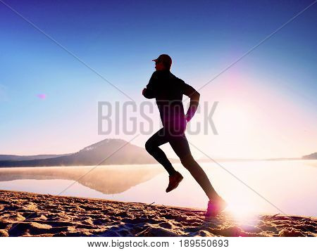 Healthy Lifestyle. Tall Young Man Runner Is Running On Sunrise Seaside. Man Jump In Sand